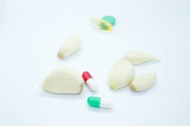 Beyaz arka planda soyulmuş sarımsak ve vitaminler var.