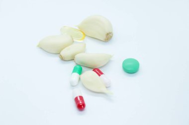 Beyaz arka planda soyulmuş sarımsak ve vitaminler var.