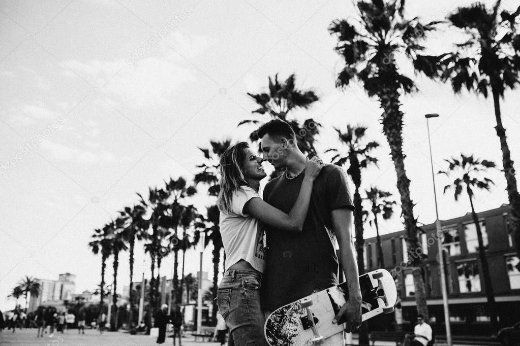 Happy young couple having fun with skateboard on the city street near the beach