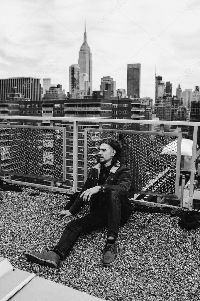 Bearded hipster sitting on rooftop in New York city, Manhattan, USA. Black and white photo