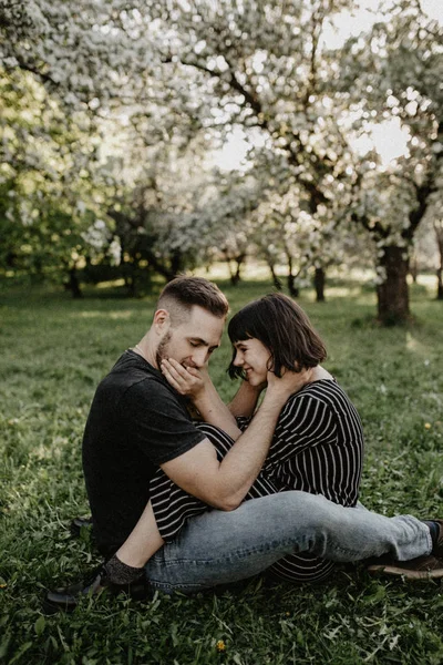 Frühlingsfreunde im blühenden Garten. Junge und Mädchen sitzen auf grünem Gras — Stockfoto