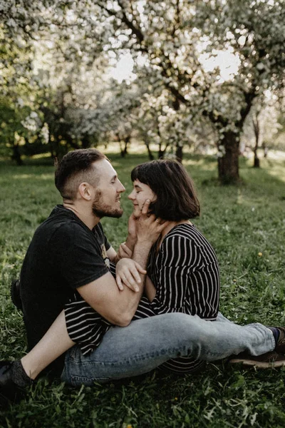 Gli amanti della primavera in giardino fiorito. Ragazzo e ragazza seduti su erba verde — Foto Stock