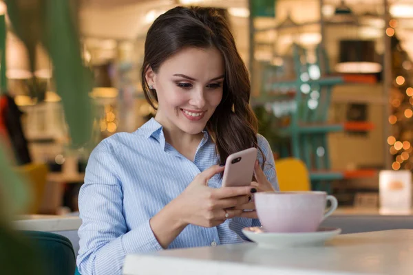Piękna ładny kaukaski młoda kobieta w kawiarni, przy użyciu telefonu komórkowego i picie kawy uśmiechający się — Zdjęcie stockowe
