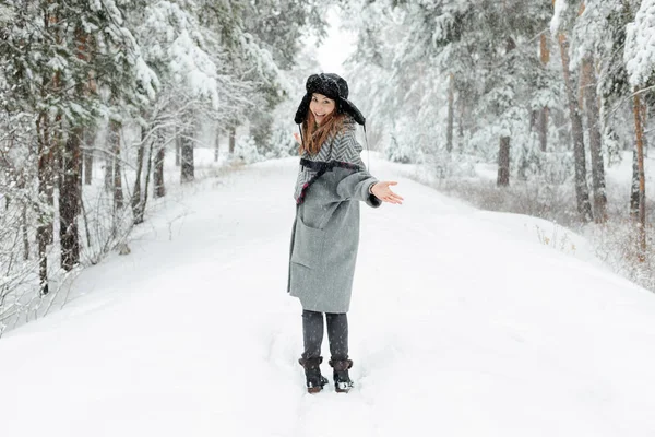 Hermosa joven de pie entre los árboles nevados en el bosque de invierno y disfrutando de la nieve . Imagen De Stock