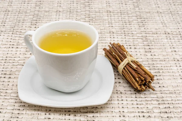 A close-up of a cup of apple tea with a patterned table cloth in the background and a bunch of cute little sticks