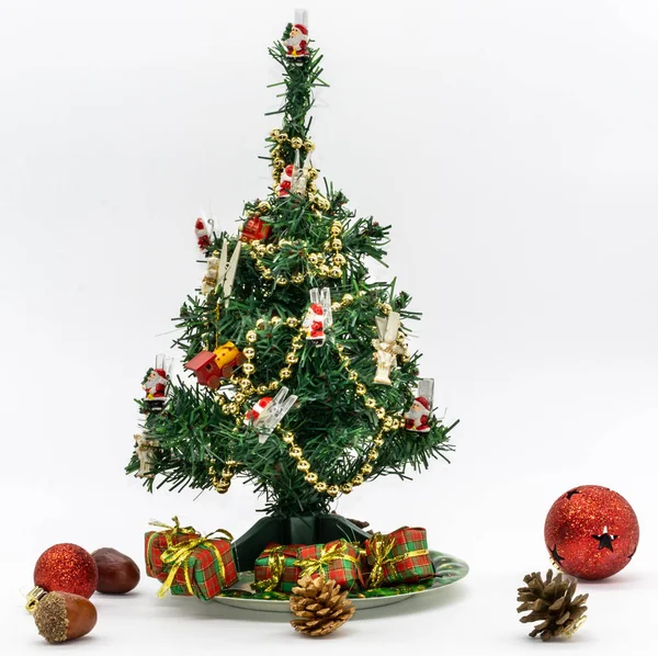 Bir tabak içinde kaidesi, bazı küçük hediyeler, Noel topları ve temiz ve beyaz arka plan ile fındık ile yeşil bir Noel ağacı görünümünü