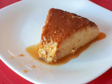 Puding kırmızı kumaş tabloya arka plan üzerinde beyaz bir plaka üzerinde şeker şurubu ile lezzetli bir parçası