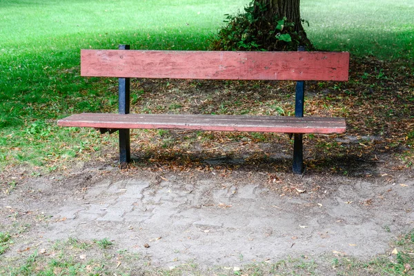 Mavi ve birisi bir ağacın arkasına ve arka planda yeşil çim oturmak için bekleyen bir kamu kare kırmızı boyalı bir rustik Bank