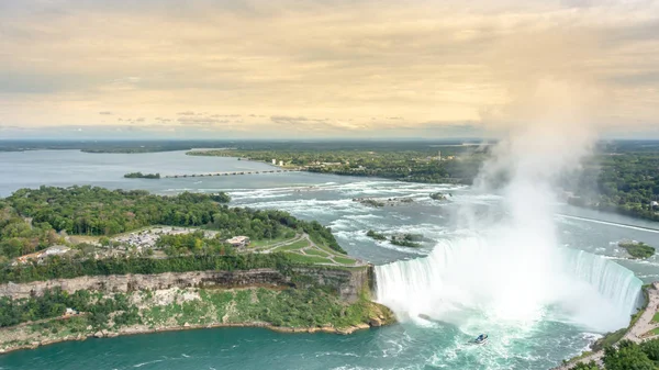 Niagara Falls, üzerinde / Kanada - 09/06/2018: Niagara Şelaleleri ile sarımsı bir gökyüzü, kaldırım ve bir tekne ile turistler şelaleyi yakınındaki boyunca yürüyüş insanlar büyük havadan görünümü