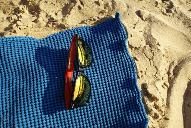 Mavi bir plajda güneş gözlüğü. Havlu..