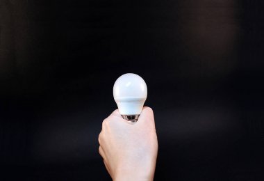 Bir el siyah bir arka plan üzerinde bir enerji tasarruflu ampul tutar.
