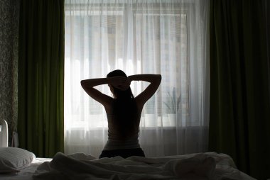 Pencerenin yanında yatakta uzun saçlı bir kızın silueti.