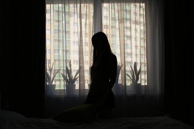 Pencerenin kenarında uzun saçlı bir kızın silueti..