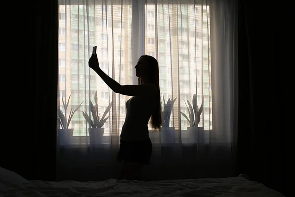 Silhouette Una Ragazza Con Uno Smartphone Vicino Alla Finestra — Foto Stock