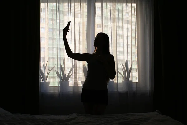 Silhouette Una Ragazza Con Uno Smartphone Vicino Alla Finestra — Foto Stock