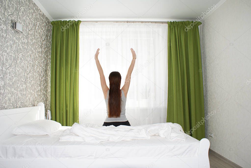 Silhouette of a girl with long hair on the bed by the window.