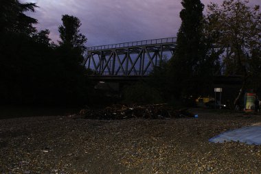 Köprünün arka planına karşı çakıl bir sahilde çöp.