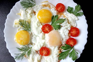 Domates ve siyah bir zemin üzerine beyaz bir plaka üzerinde otlar pişmiş yumurta
