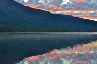 Göl üzerinde gündoğumu. Pembe bulutlar yükselen güneş tarafından boyalı gölün suya yansıyan.