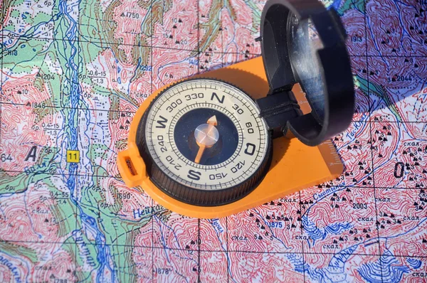 Open magnetic compass with mirror cover is lying on a topographic map.