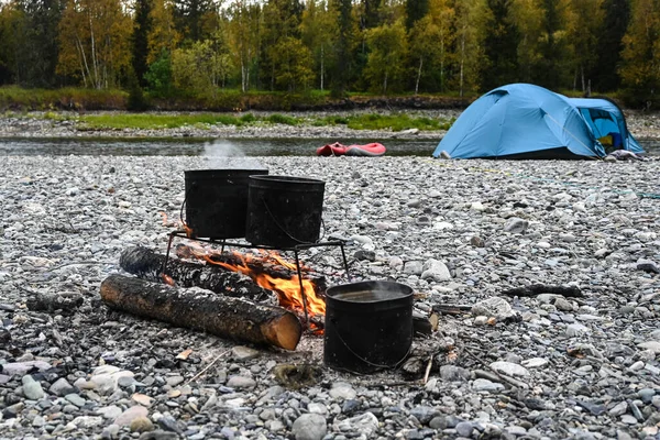 Camp fire. Fire with pots on the background of tent and boats.