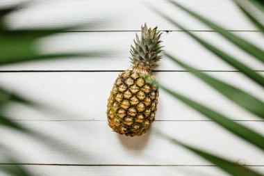 Olgun ananas, palm çerçeve beyaz ahşap zemin üzerine bırakır. Tropikal meyve yaratıcı kavramı.