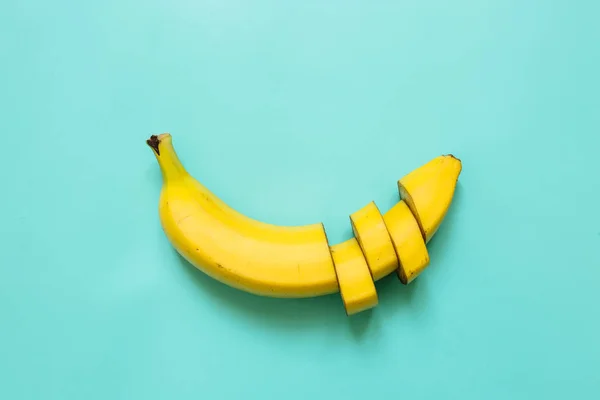 Cut banana, slices, dices arranged on cyan green, blue, ultramarine background. Room for text. Minimalist concept.