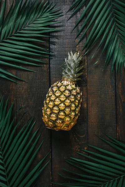 Olgun ananas, palm çerçeve koyu ahşap arka plan üzerinde bırakır. Tropikal meyve yaratıcı kavramı.
