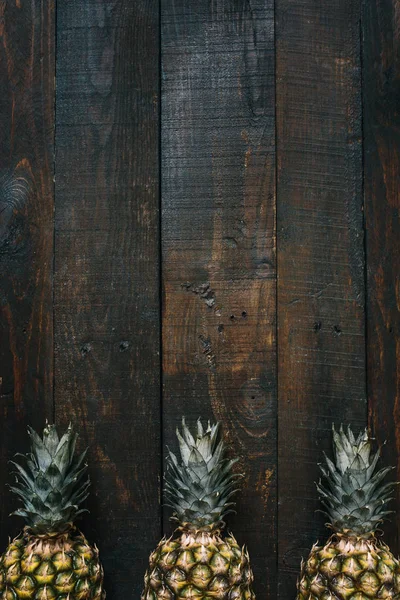 Olgun ananas sınır çerçeve koyu ahşap dikey arka plan üzerinde. Tropikal meyve yaratıcı kavramı. Kopyalama, metin, yazı için boş alan.