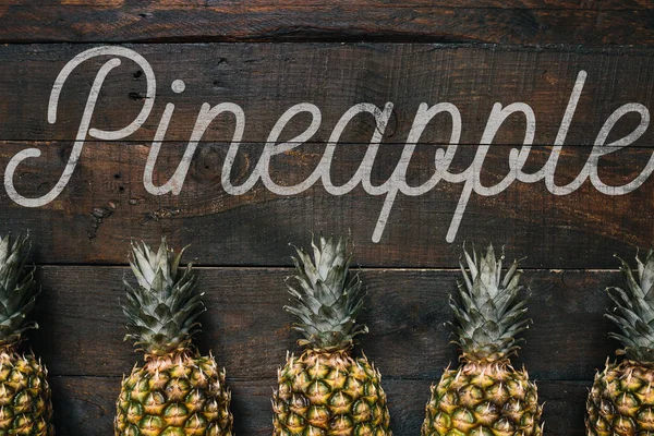 Pinapple message, text, lettering. Ripe pineapples border frame on dark wooden rustic background.