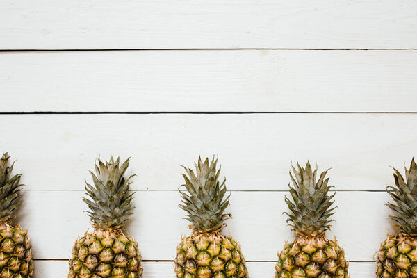 Ripe pineapples border frame on white wooden background. Tropical fruit creative concept. Room for copy, text, lettering.