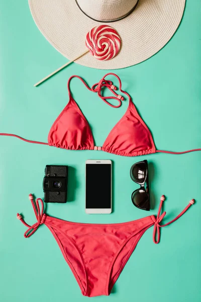 Kırmızı, pembe bikini takım, lolipop, güneş gözlüğü, smartphone, ince tabaka fotoğraf makinesi, düz açık mavi renkli şapka. Yaz tatil kavramı. Dikey tropikal poster, kartpostal.