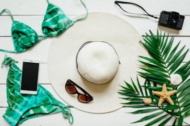 Bikini takım elbise, şapka, güneş gözlüğü, film kamerası, smartphone, deniz yıldız, yeşil plam ahşap baclground görücü usulü bırakır. Yaz tatil tatil kavramı.