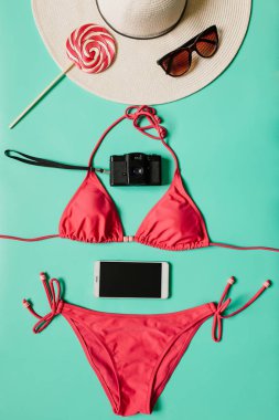Kırmızı, pembe bikini takım, lolipop, güneş gözlüğü, smartphone, ince tabaka fotoğraf makinesi, düz açık mavi renkli şapka. Kopyalama, metin, yazı için boş alanı. Dikey yaz tatil kavramı.