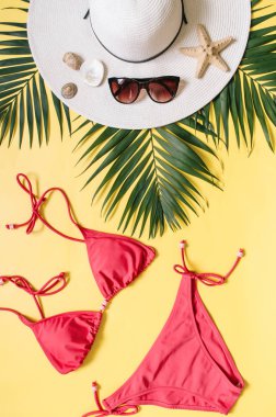 Plaj giyim ve tropikal yaprak sarı zemin üzerine düzenlenmiştir. Yaz tatil minimalist tarzda kavramı.