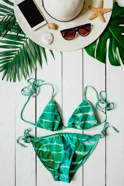 Bikini takım elbise, şapka, güneş gözlüğü, smartphone, deniz yıldız, yeşil plam ahşap baclground görücü usulü bırakır. Yaz tatil tatil kavramı. Dikey tropikal poster afiş, kartpostal.