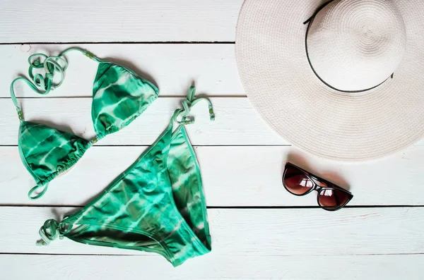 Green bikini suit, hat, sunglasses, sea star arranged on wooden baclground. Summer holidays vacation concept. Tropical poster banner, postcard.