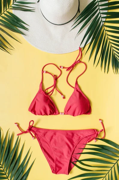 Plaj giyim ve tropikal yaprak sarı zemin üzerine düzenlenmiştir. Yaz tatil minimalist tarzda kavramı.