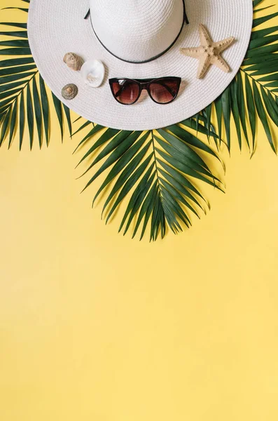 Straw hat, sunglasses and tropical palm leaves arranged on plain yellow background. Tropical vacations concept. Empty space for copy, text.