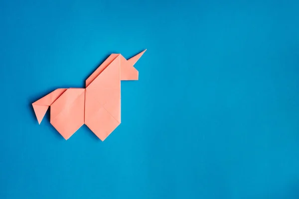Handmade pink trendy geometrical polygonal paper origami unicorn on blue background. Empty space. Horizontal poster, postcard, banner template.
