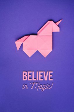 Ultraviyole arka plan olarak el yapımı pembe trendy geometrik origami tek boynuzlu at. Sihirli metin, mektup, yazı, teklif inanıyorum. Dikey poster, kartpostal, afiş.