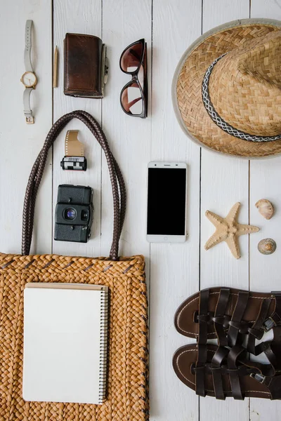 Kadının Akdeniz turistik aksesuarlar beyaz ahşap masa arka plan düz üzerinde yatıyordu. Sarı organik saman Eko çanta, şapka, kahverengi deri sandalet, izle, retro film kamerası. Kopya için boş defter alanı.