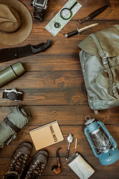 Camping gear including knife, clothes, boots, lantern, camera, hat, map, compass. Vertical wanderlust, safari postcard, poster, banner template. Room for text,copy, lettering.