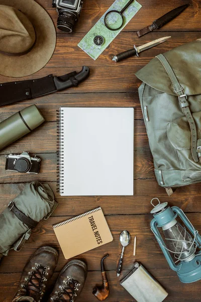 Camping gear including knife, clothes, boots, lantern, camera, hat, map, compass. Vertical wanderlust, safari postcard, poster, banner template. Empty notepad space for text,copy, lettering.