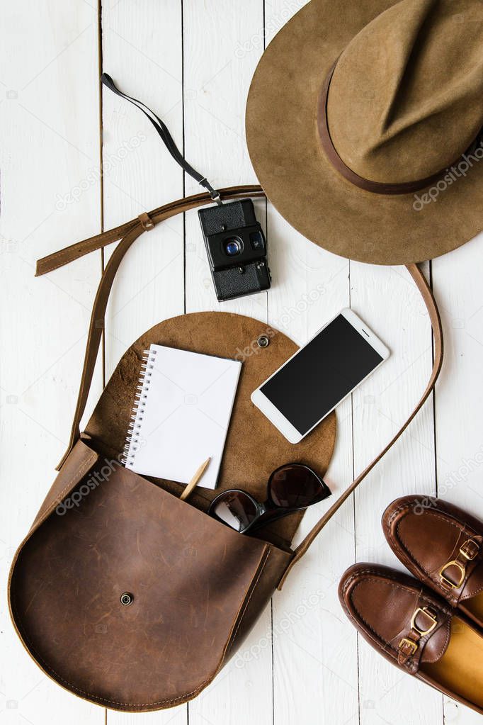 Woman's journalist or traveler accessories on white wooden table background flat lay. Brown leather purse, marine shoes, camera, cellphone, notebook, pencil, film camera. Empty space for lettering.