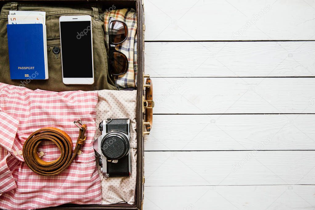 Vintage hipster clothes, shoes, hat, smartphone, accessories packed in suitcase on white wooden table. Travel concept. Empty space for copy, text, lettering.