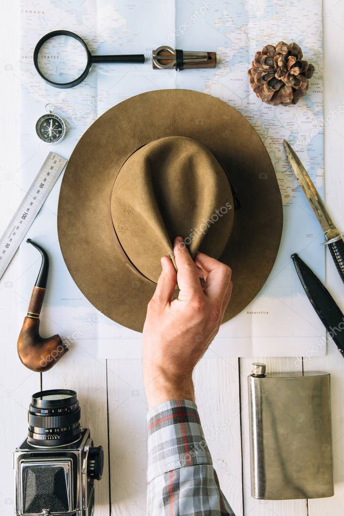 Adventure planning flat lay. Travel vintage gear on map. Traveler, explorer hands in frame taking or puting hat. Vertical exploring, hiking empty space poster, postcard concept.