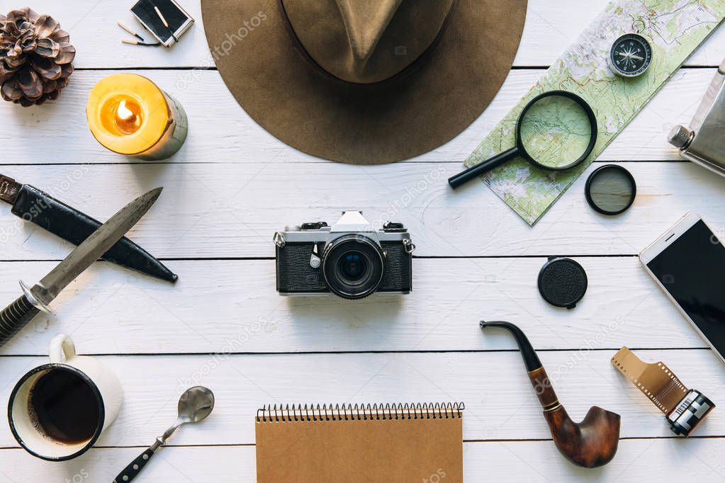 Adventure planning flat lay. Travel vintage gear on white wooden table. Including film camera, hat, knife, loupe, compass. Exploring, hiking poster, postcard, template. Empty space for copy, text, lettering.