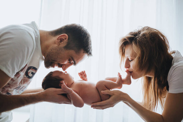 Счастливые веселые здоровые улыбающиеся родители, держащие обнаженного ребенка. Подсветка
.