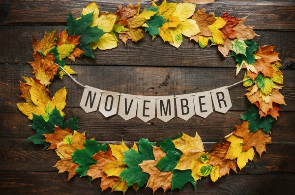 November lettering on paper cardboard eco garland, autumn leafs wreath, dark brown rustic barn wood background.